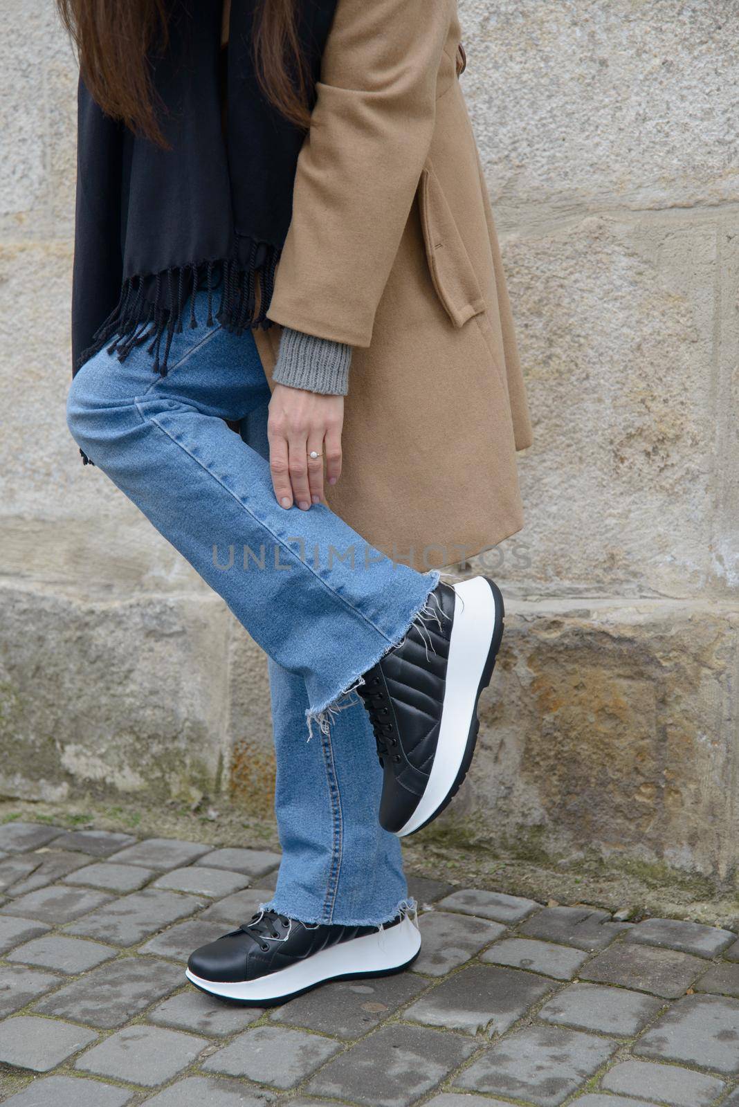 Stylish young girl posing. She is wearing a beige coat, jeans and stylish leather sports shoes.