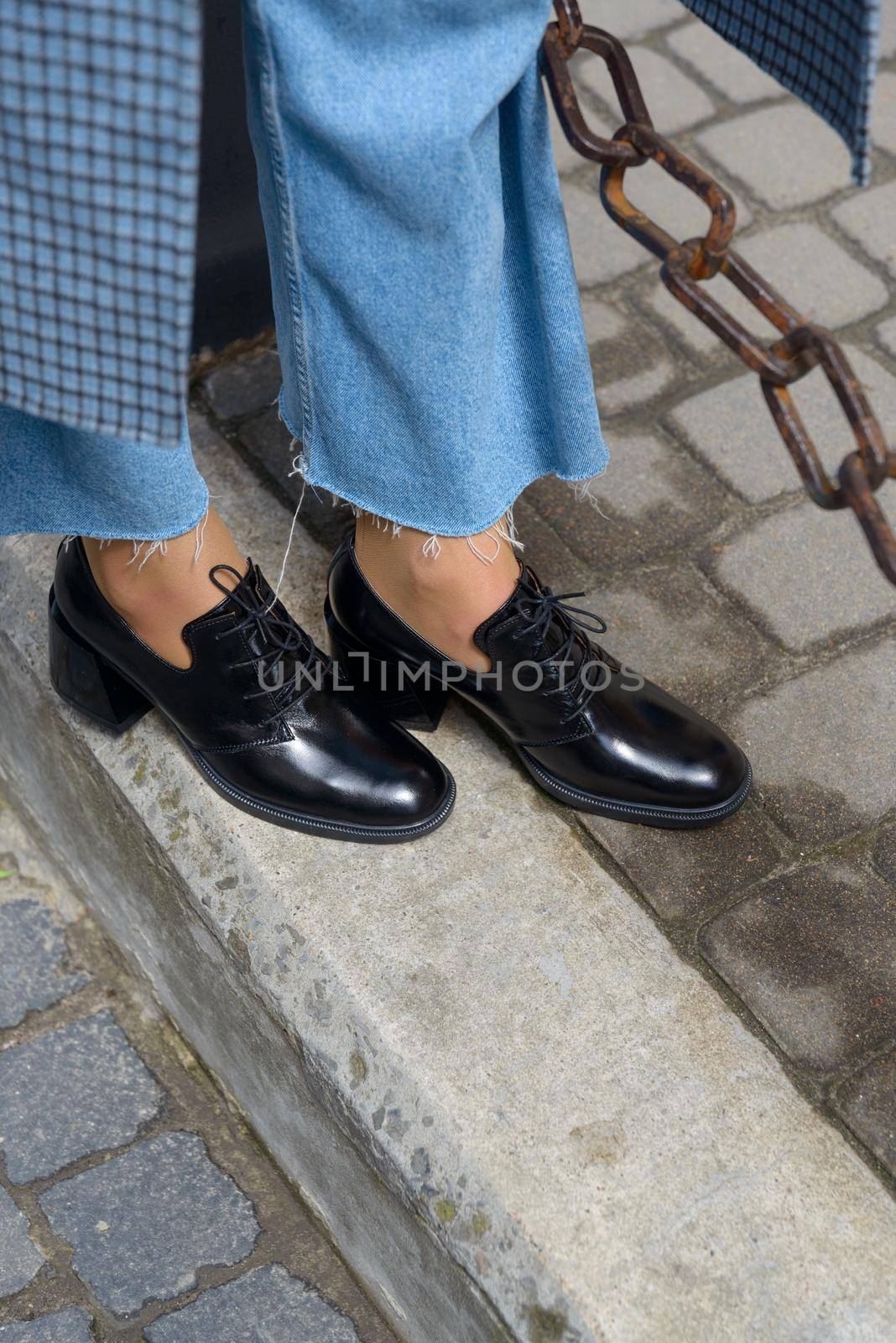 Women's leather boots close-up. The girl walks in black shiny oxford style shoes.