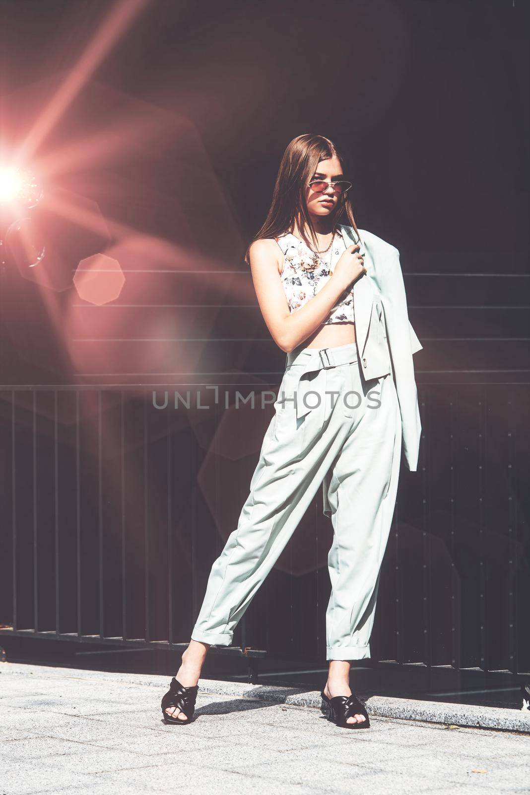 Fashion portrait of young woman wearing sunglasses, top, slingbacks, blue suit. Young beautiful happy model posing near gray metal grid by Ashtray25