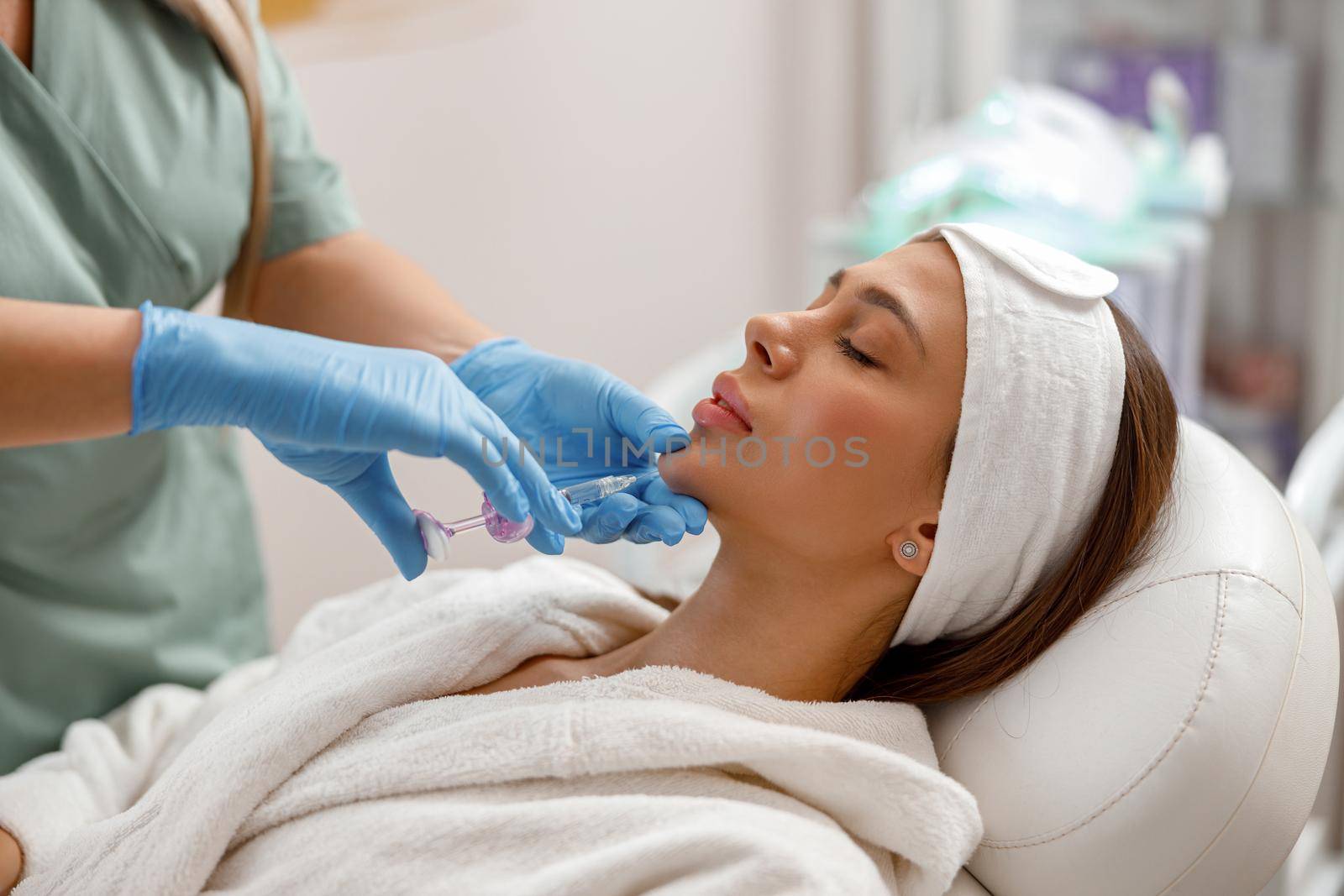 Beautiful young woman receiving hyaluronic acid injection in chin at beauty salon.