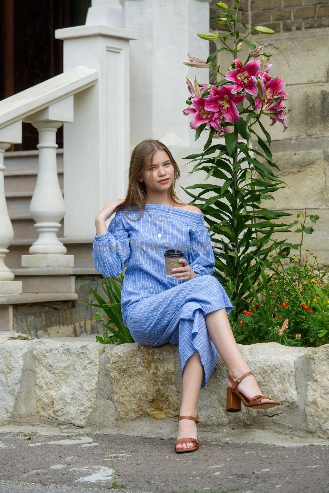 A female posing near flower on a stone curb while drinking coffe. Girl wearing a striped jumpsuit by Ashtray25