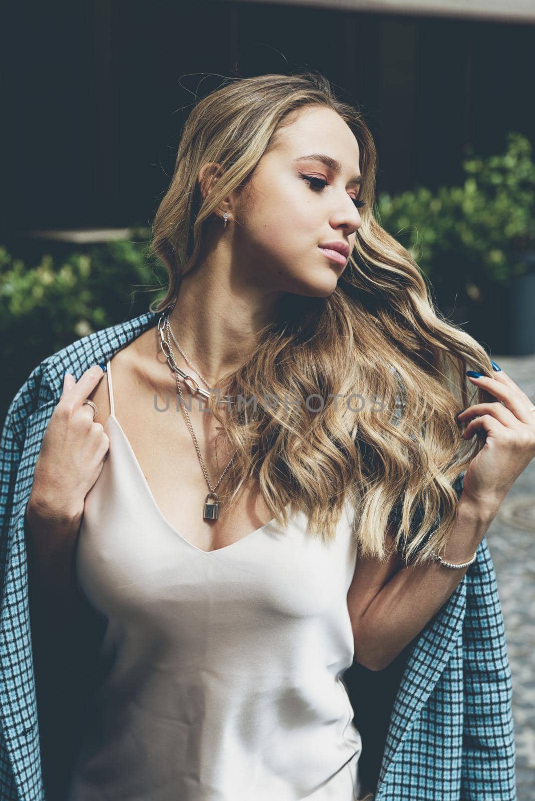 Fashionable young woman with blond hair dressed in beige dress and checkered coat posing. Street style.