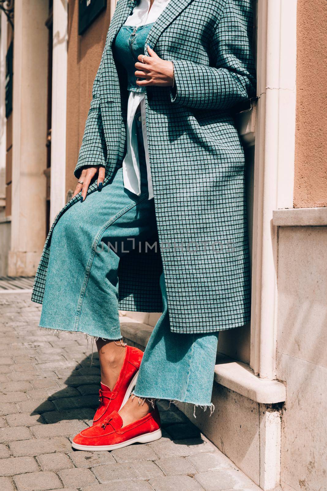 Woman in a red stylish suede loafer shoes, blue jeanse, white shirt and trendy checkered coat. Pair of trendy female loafers shoes, outdoors