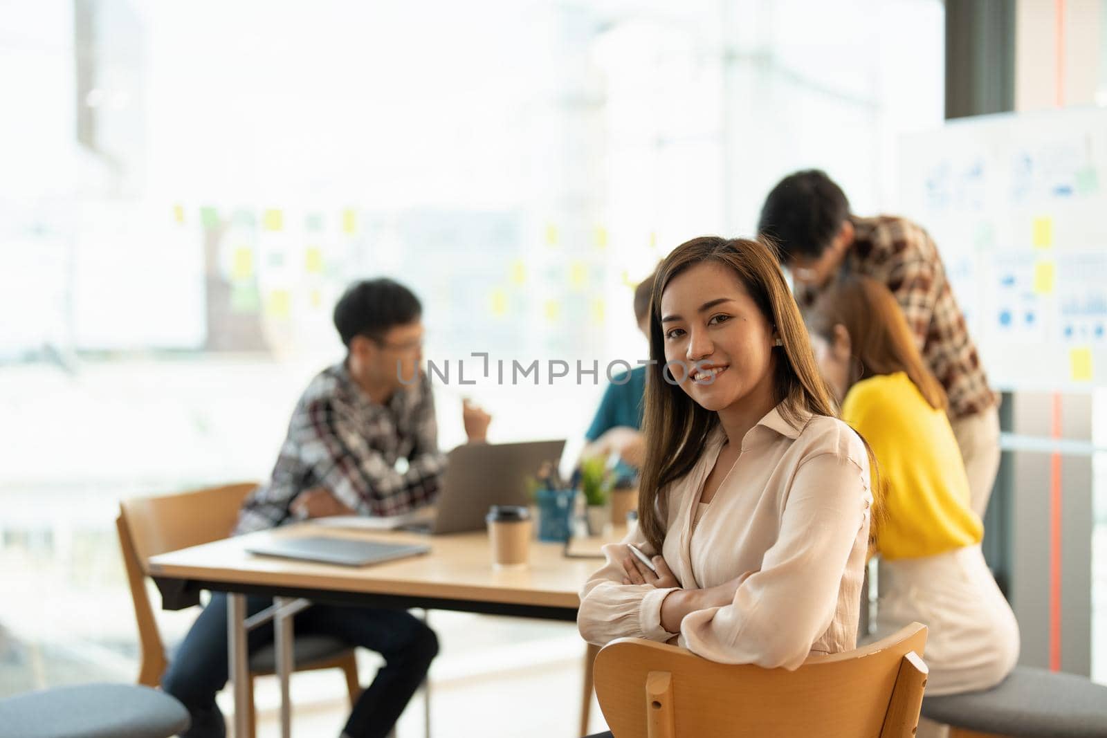 Attractive young Asian business woman smiling and looking over shoulders at business meeting with co-workers by nateemee