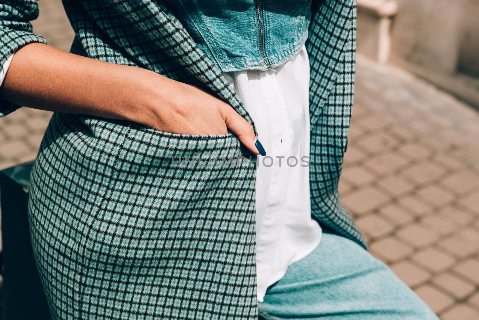 beautiful female tanned hands with blue manicure and element of stylish checkered coat