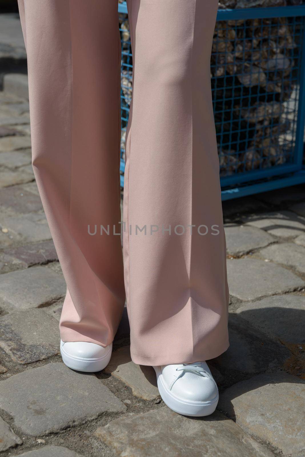 Stylish woman in fashion white sneakers shoes and beige trousers walks around the city. Close-up.