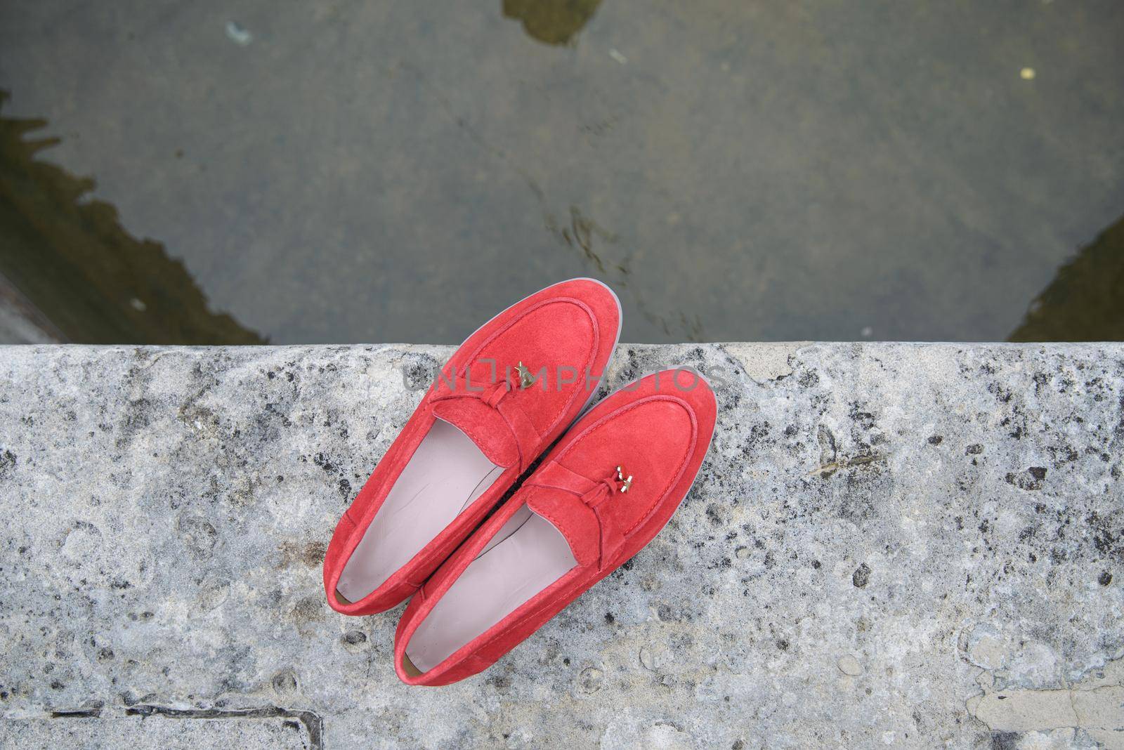Woman's red stylish suede loafer shoes on the stone background. Pair of trendy female loafers shoes, outdoors by Ashtray25