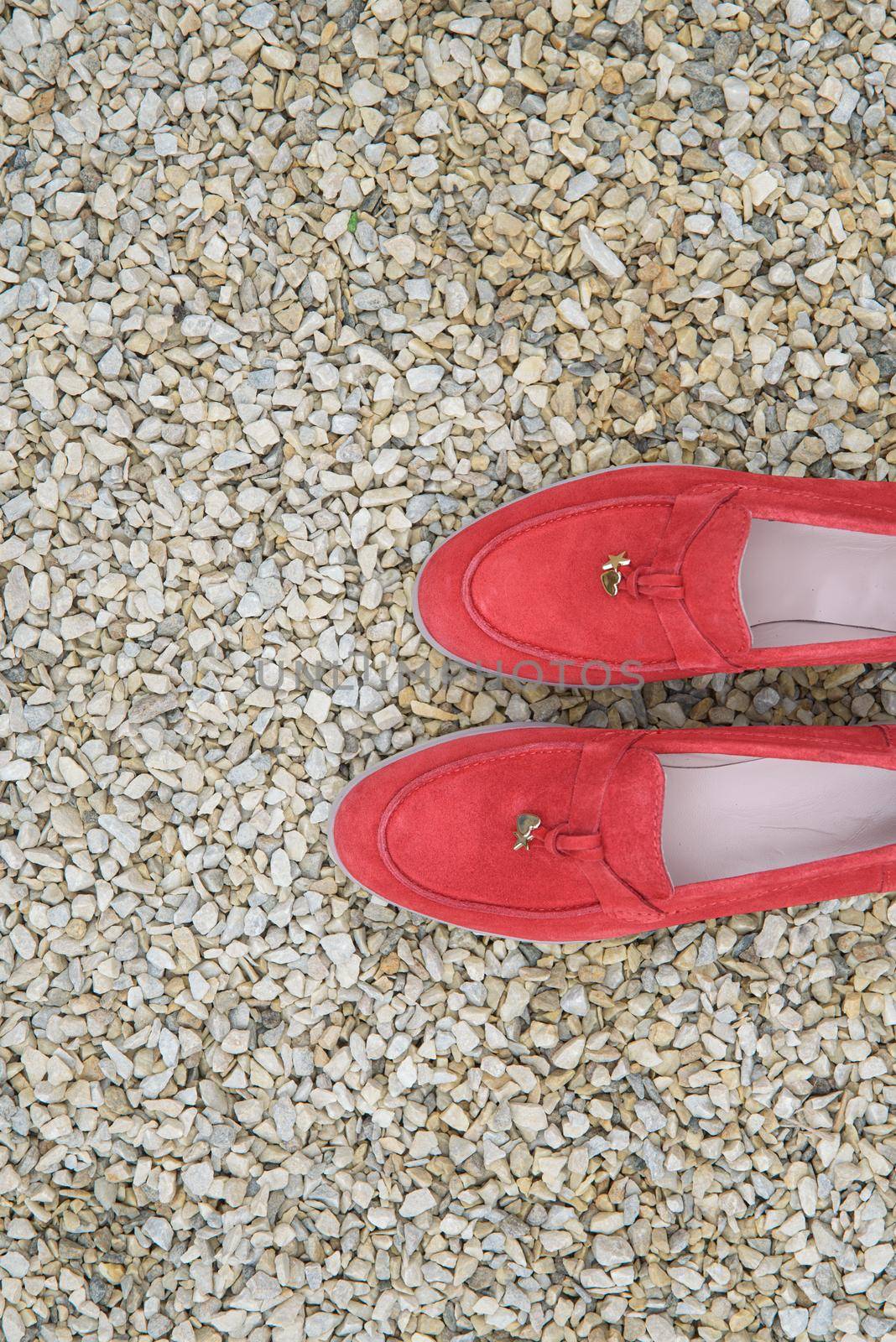 Woman's red stylish suede loafer shoes on the stone background. Pair of trendy female loafers shoes, outdoors.