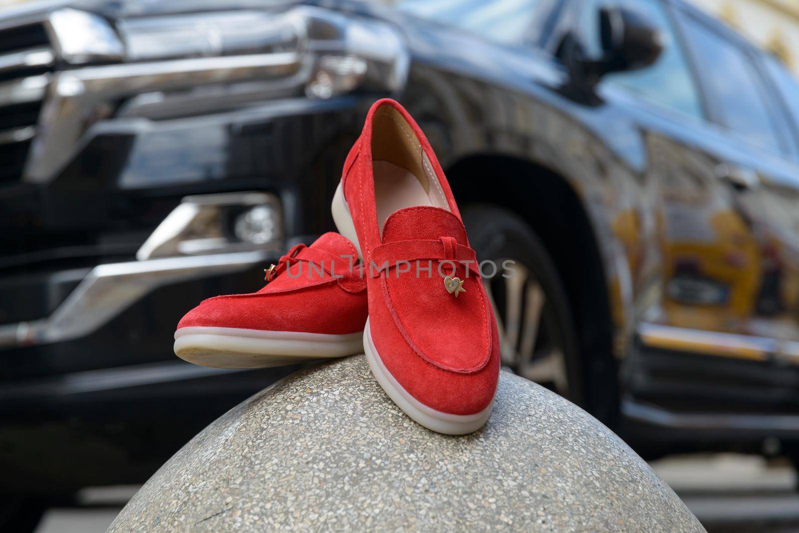 Woman's red stylish suede loafer shoes on a stone, car on a background. Pair of trendy female loafers shoes by Ashtray25