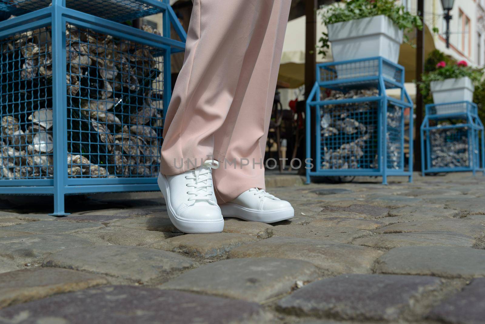 Stylish woman in fashion white sneakers shoes and beige trousers walks around the city. Close-up.