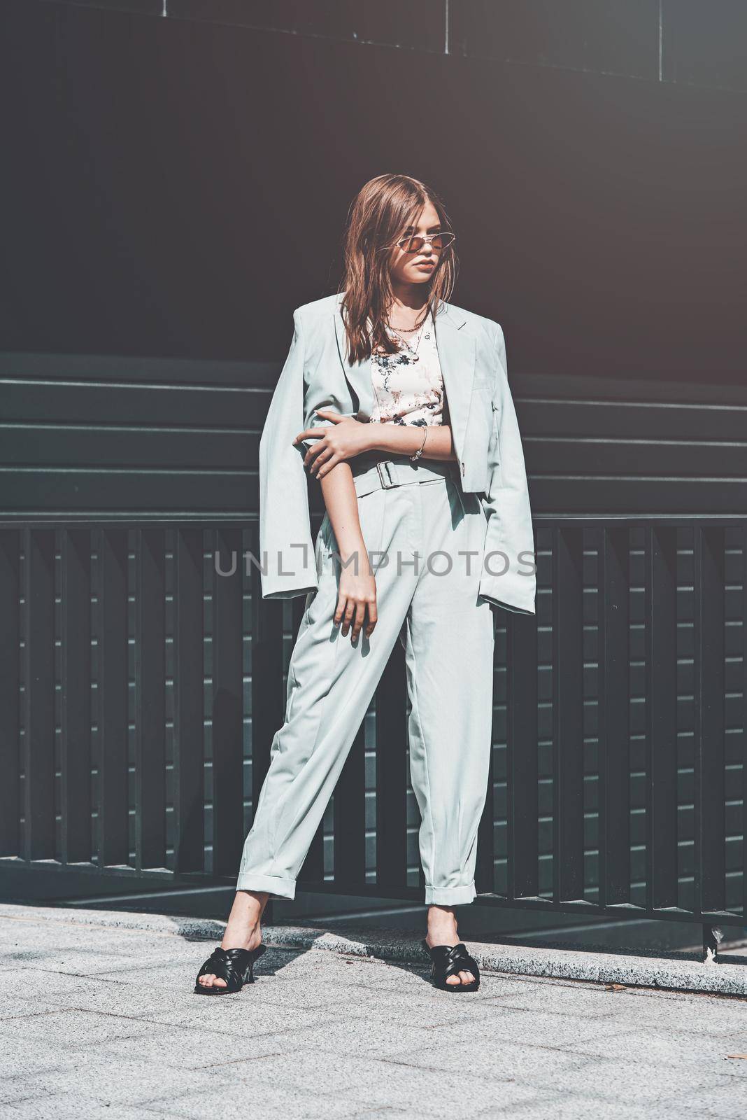Fashion portrait of young woman wearing sunglasses, top, slingbacks, blue suit. Young beautiful happy model posing near gray metal grid by Ashtray25
