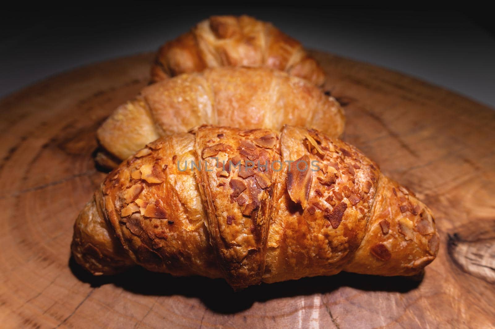 Close-up of a pile of three croissants on a wooden board against a dark background. Delicious and healthy breakfast.