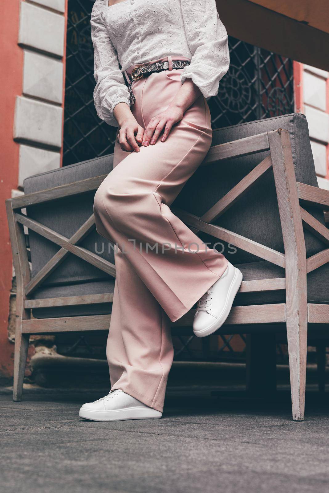 Stylish woman in fashion white sneakers shoes and beige trousers walks around the city. by Ashtray25