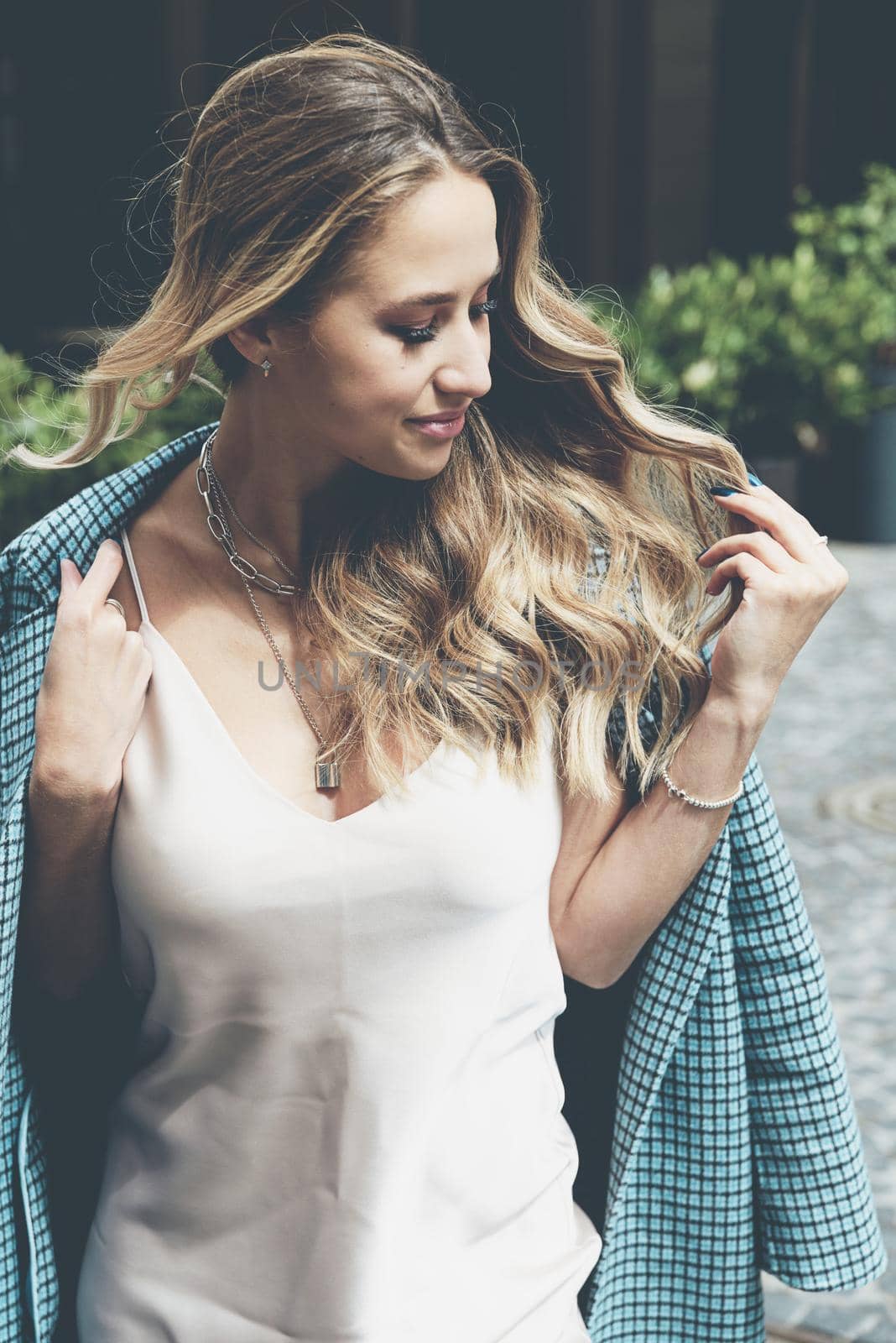 Fashionable young woman with blond hair dressed in beige dress and checkered coat posing. Street style.