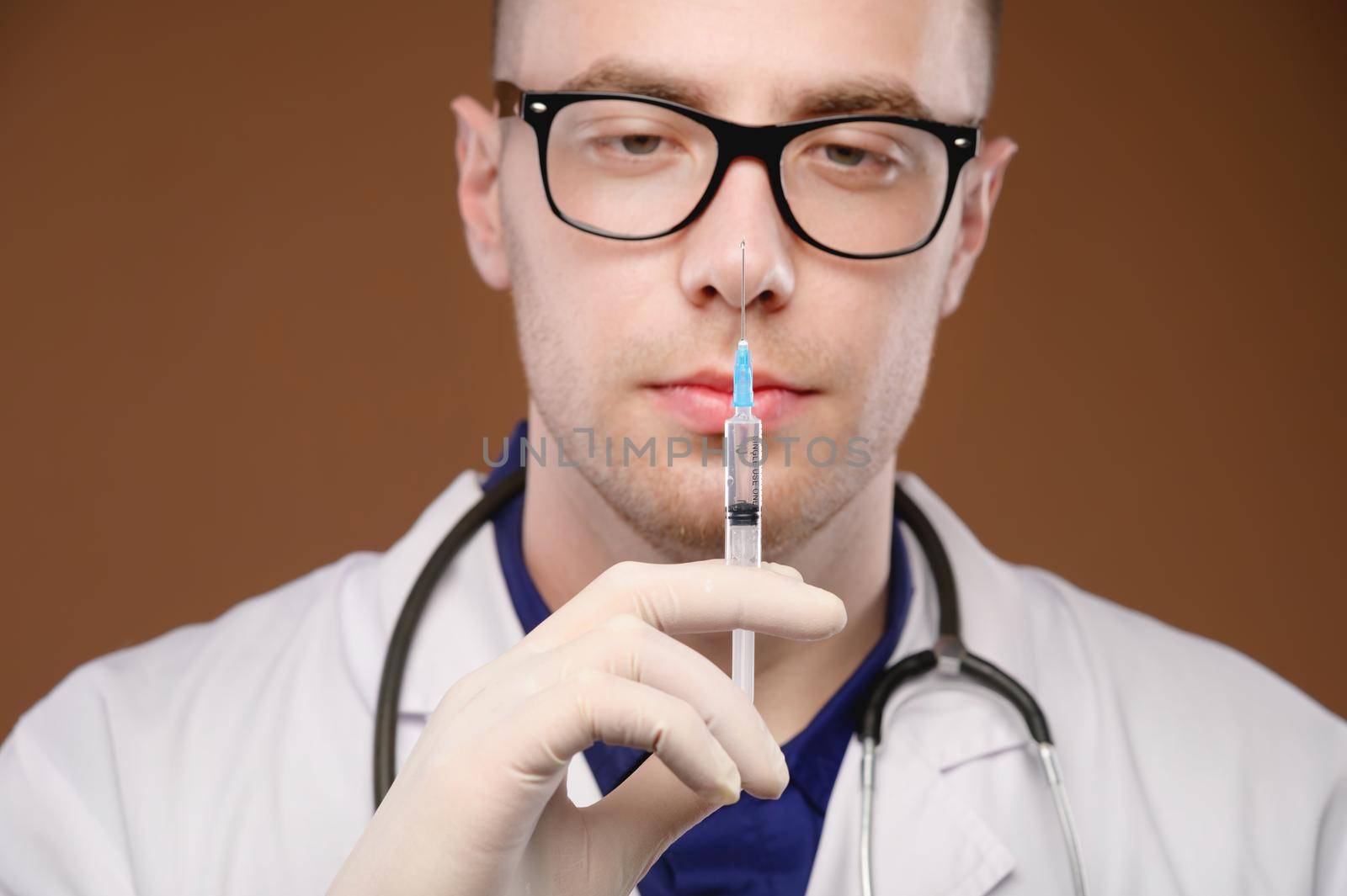 Studio portrait of a male doctor in a white coat with a syringe and an ampoule of a vaccine in his hands. Caucasian doctor on brown background.
