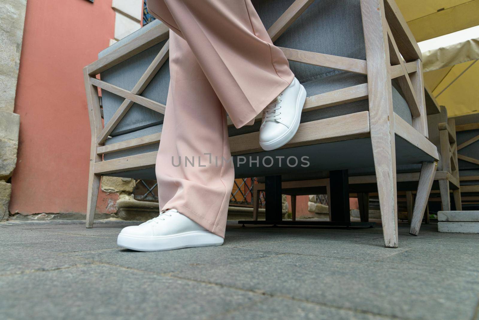 Stylish woman in fashion white sneakers shoes and beige trousers walks around the city. Close-up.