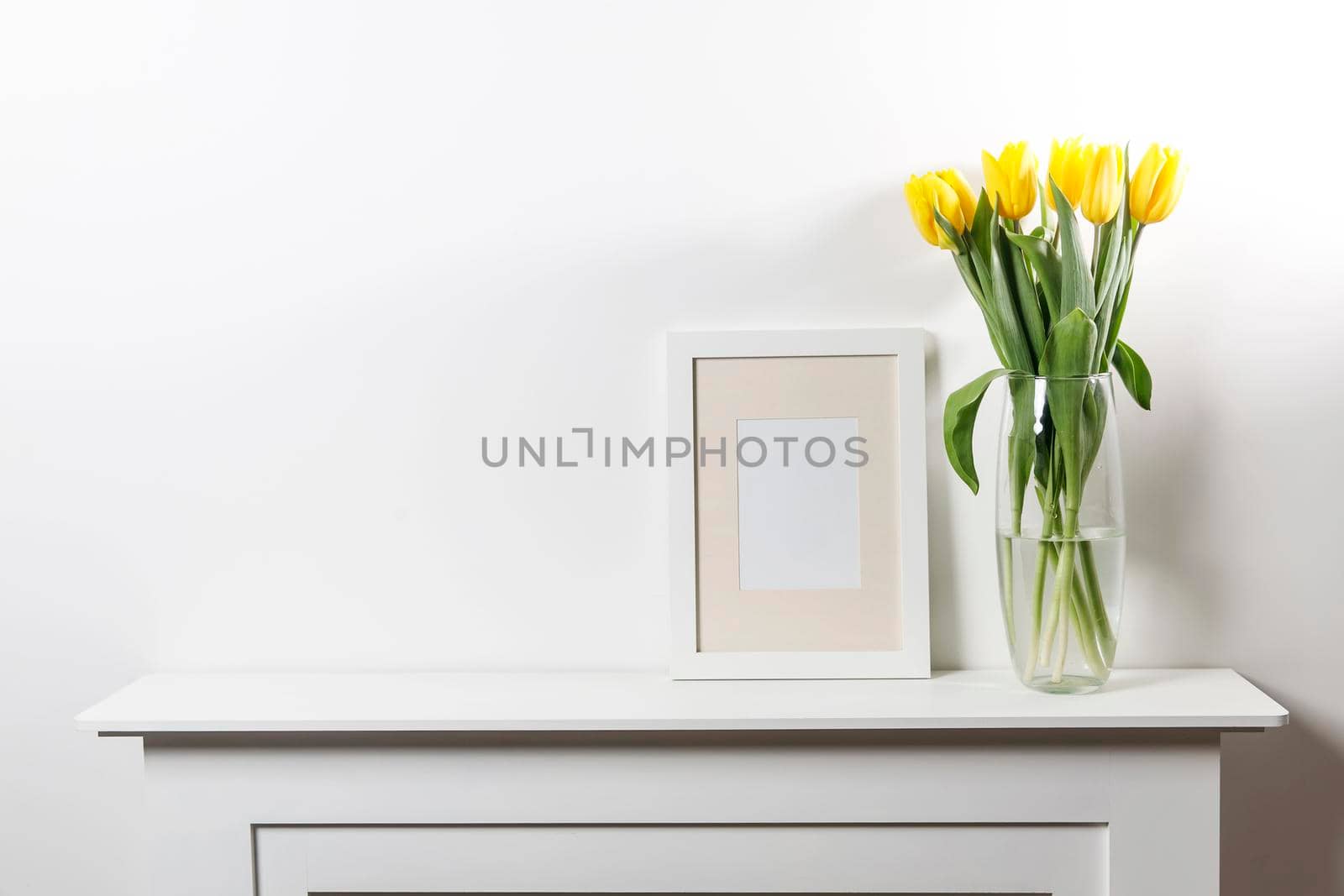 Bouquet of yellow tulip in the glass vase on white table