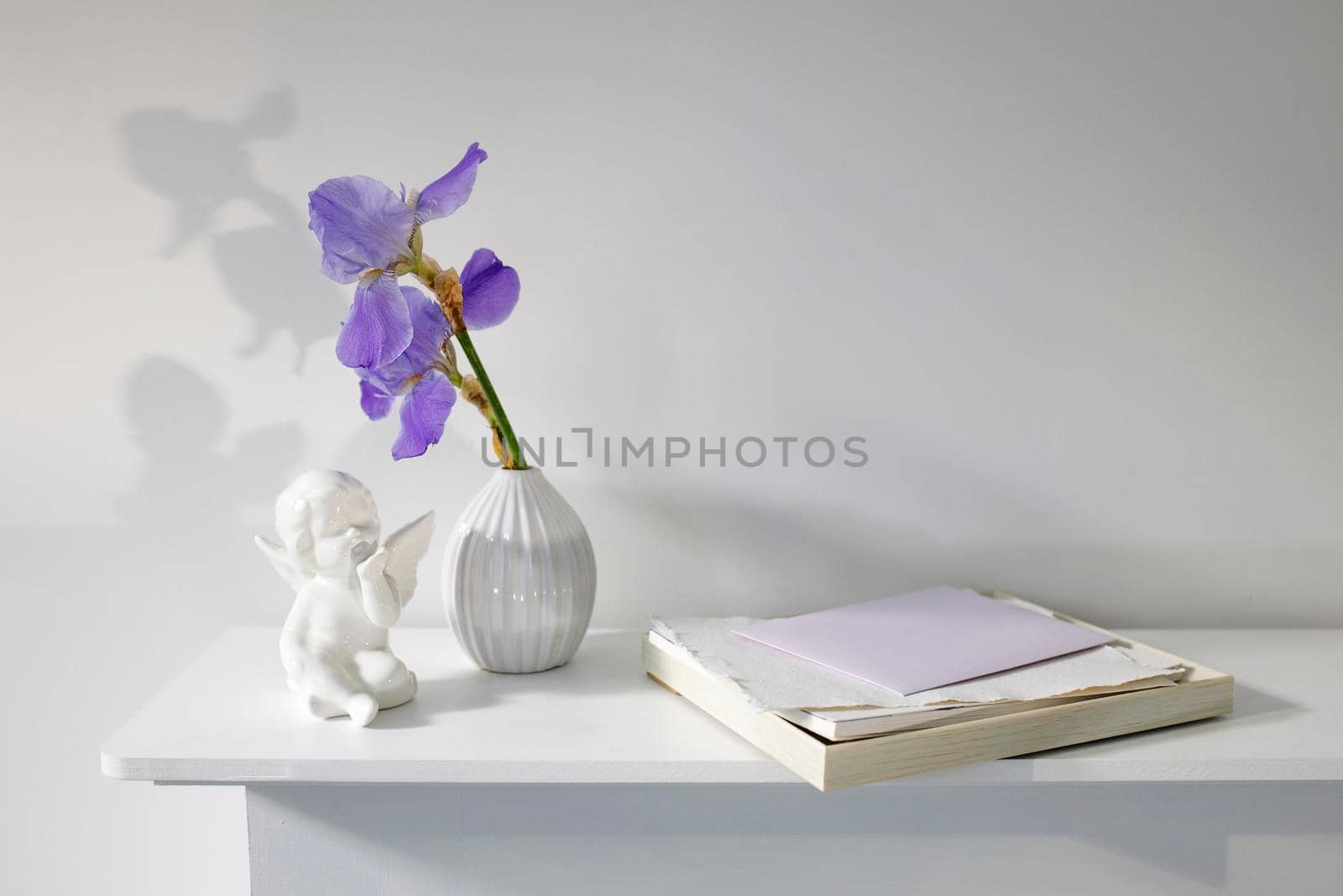 Blue iris in a corrugated vase with a piece of craft paper on a white table. Figurine of the angel. Place for text by elenarostunova