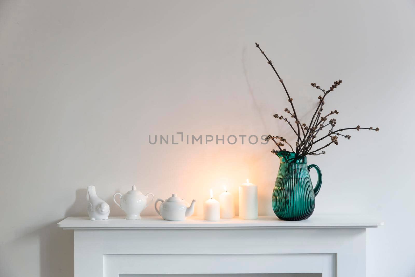 American maple branches in a green glass jar, porcelain cups, figurines, teapot on a white chest of drawers. Scandinavian style by elenarostunova