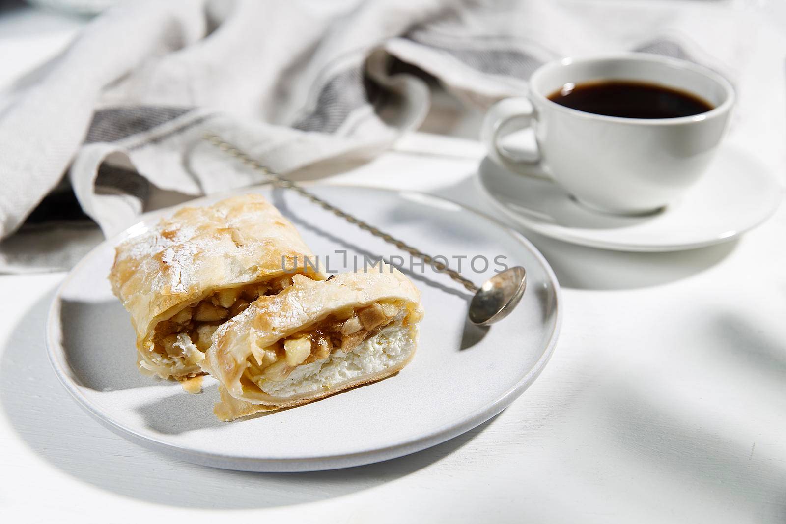 Apple charlotte with cottage cheese cream on a porcelain plate and a cup of tea on the table.