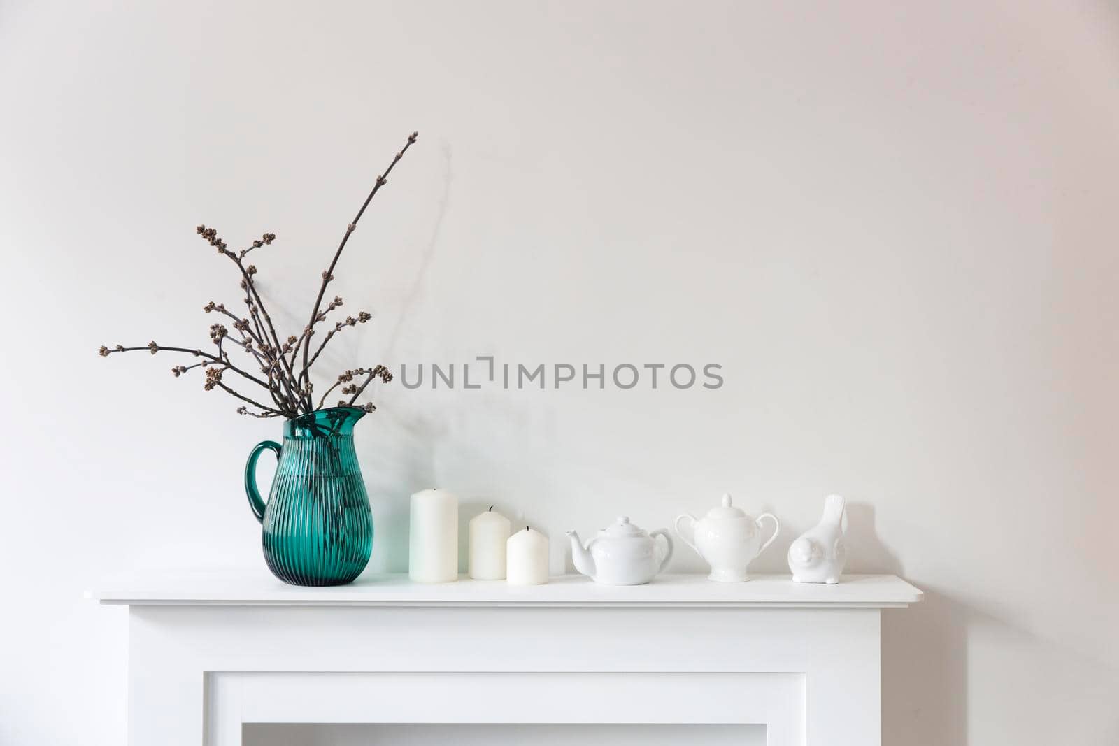 American maple branches in a green glass jar, porcelain cups, figurines, teapot on a white chest of drawers. Scandinavian style by elenarostunova