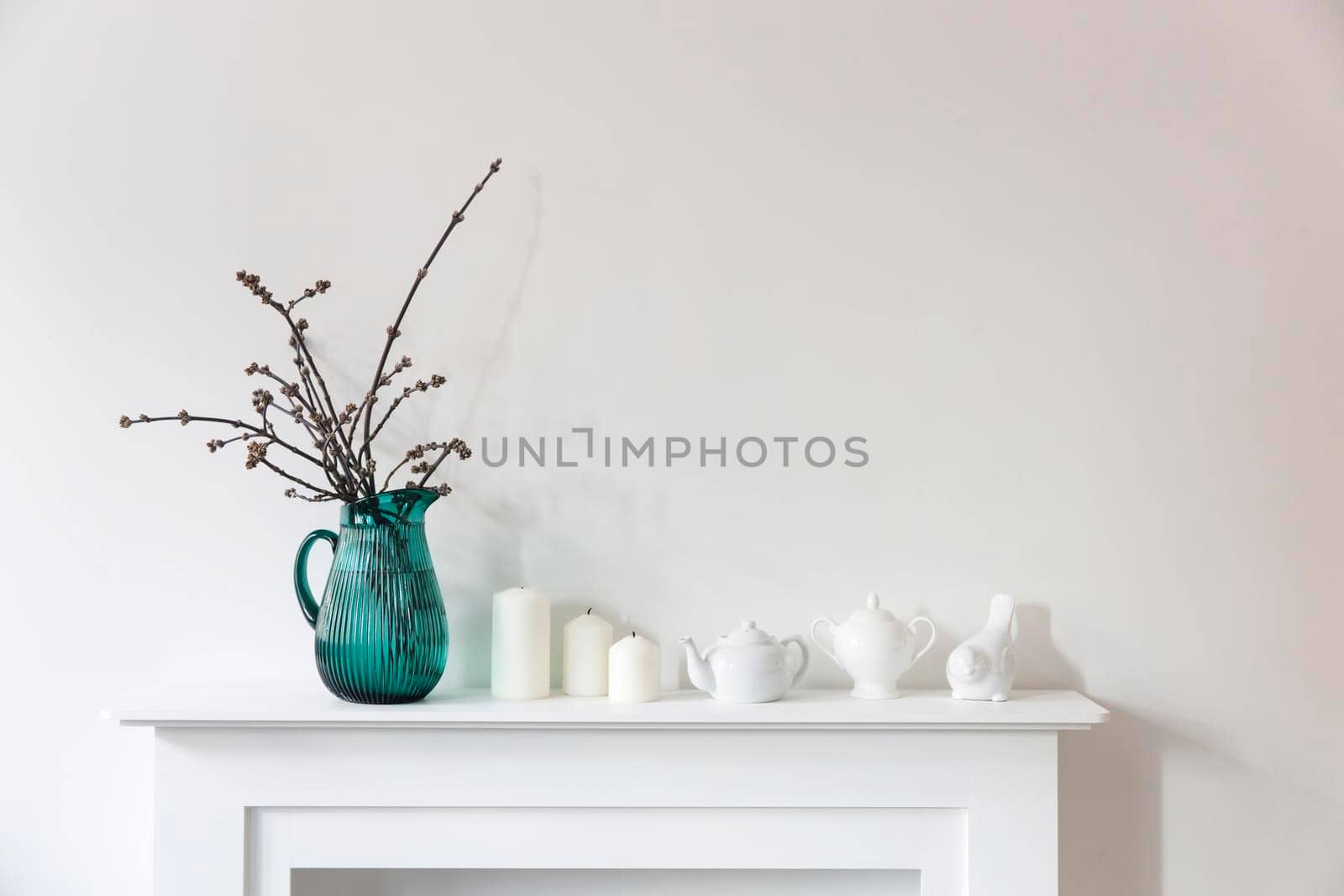 American maple branches in a green glass jar, porcelain cups, figurines, teapot on a white chest of drawers. Scandinavian style