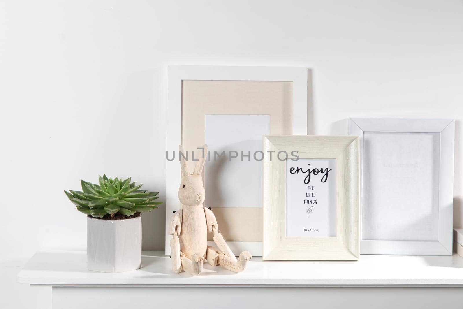 Echeveria in a geometric vase, photo frames and a wooden hare on a chest of drawers against a white wall. Scandinavian style. Ready layout. by elenarostunova