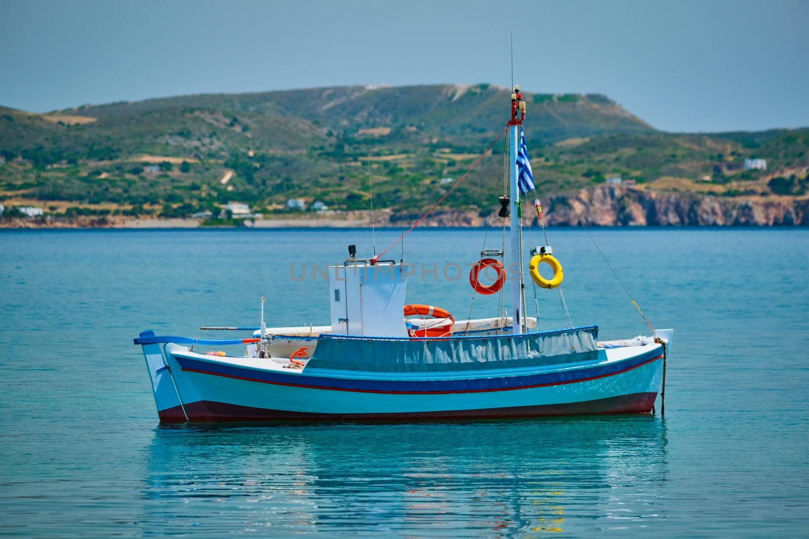 Greek fishing boat moored in blue waters of Aegean sea in harbor of near Milos island, Greece