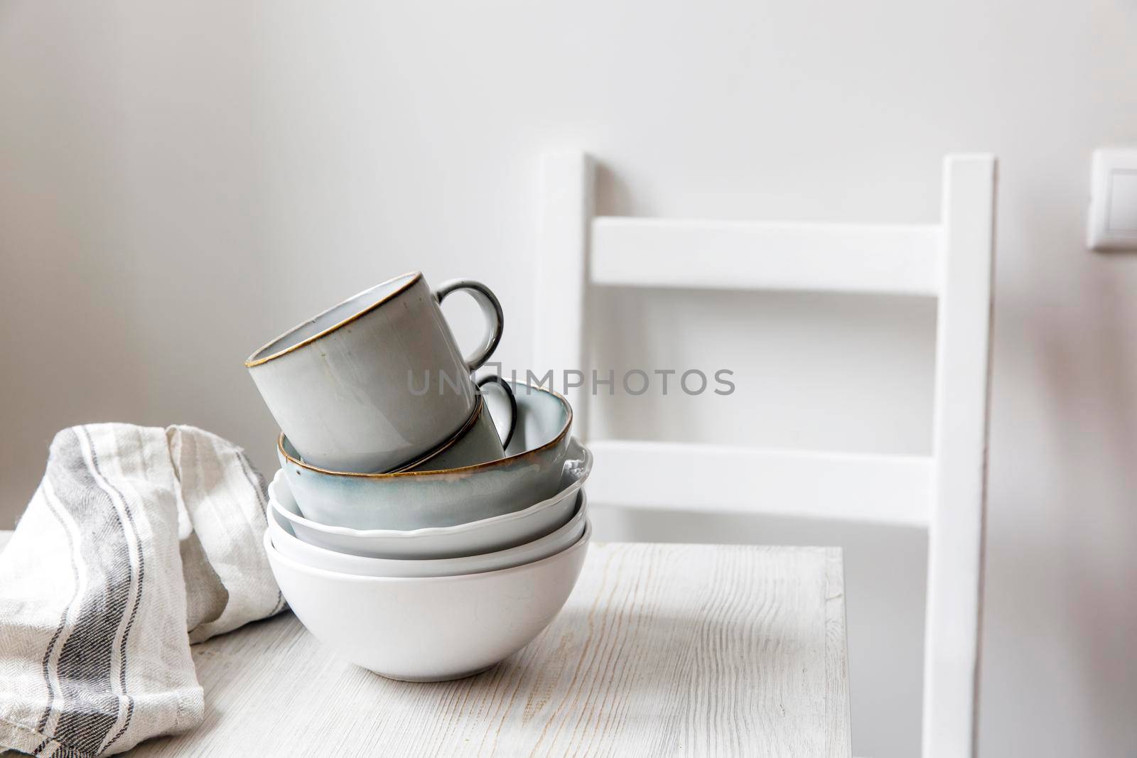 A pyramid of white bowls, plates and cups of different sizes and colors on a beige table in the kitchen. Scandinavian style. Place for your text. Copy space by elenarostunova