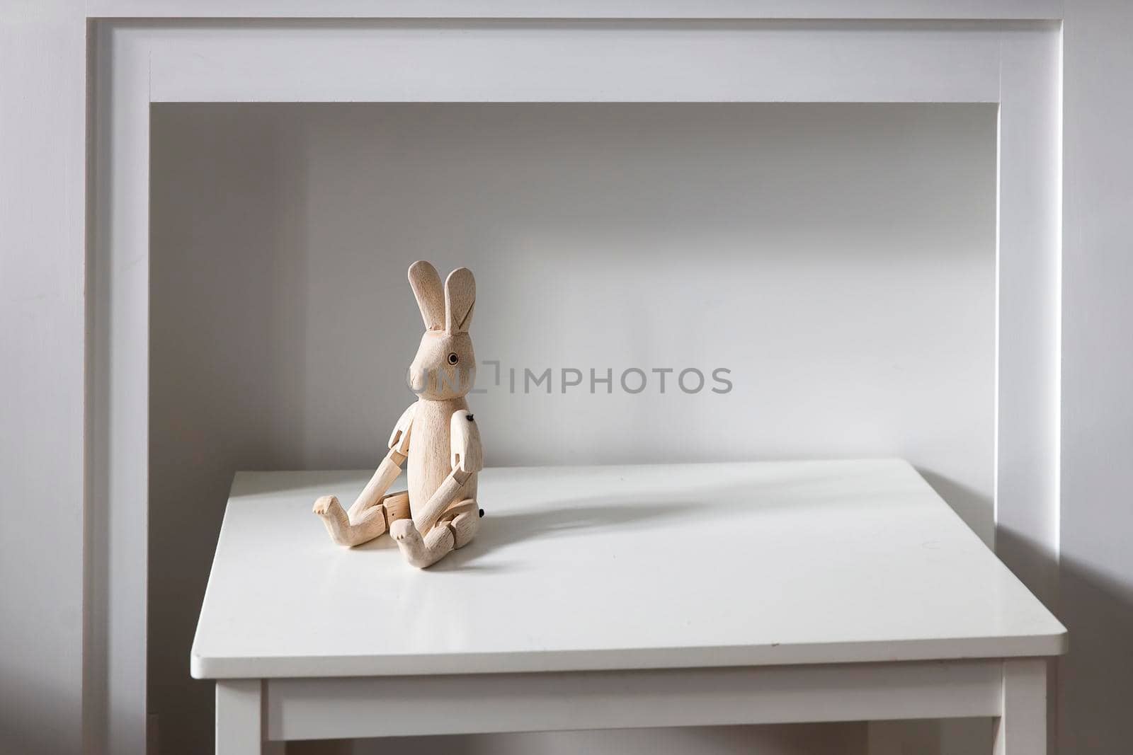 An unpainted wooden hare on hinges is on a white table in front of a fake fireplace. Place for text