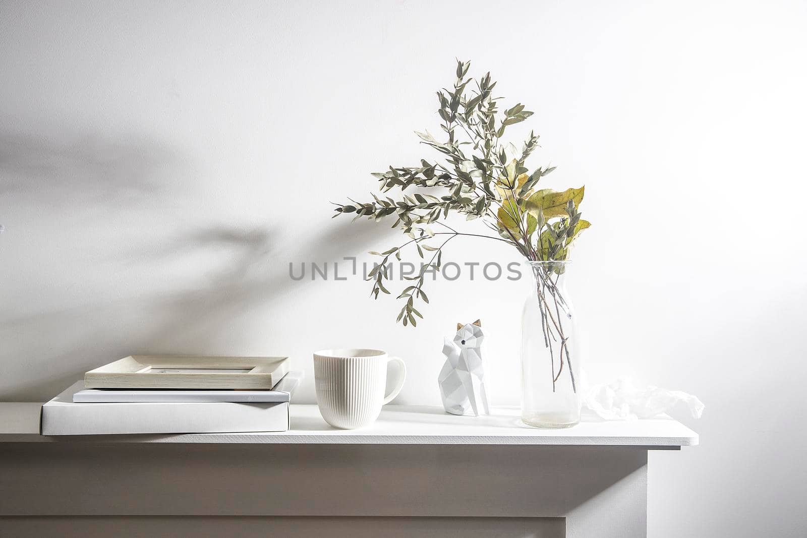 Dry eucalyptus branches in a ceramic vase, a modern fox figurine, photo frames, a notebook and a crumpled sheet of paper on a white background. Scandinavian style.