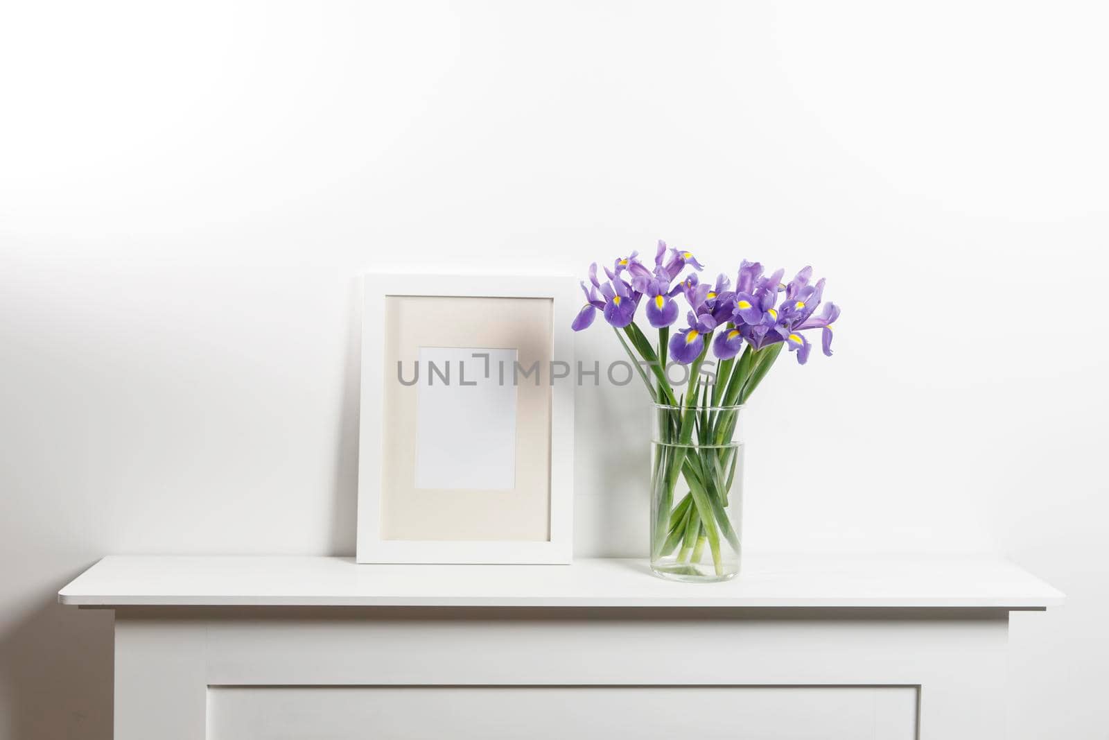Bouquets of irises in a vase, photo frames on a chest of drawers
