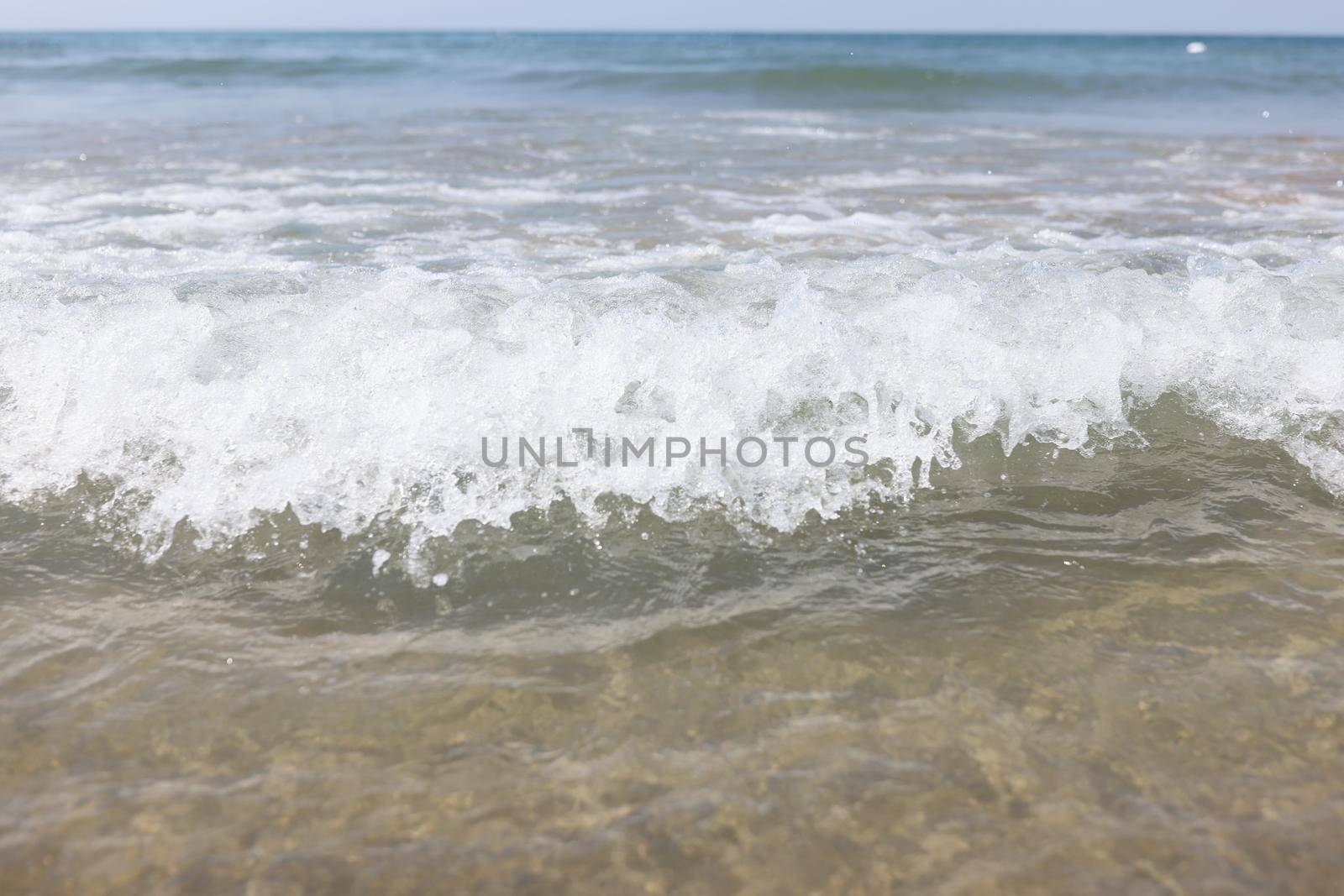 Close-up of blue sea waves, sandy coastline, choppy sea, clean water. People on horizon swimming in water. Beach, ocean, black sea, holiday, summer, relaxation concept