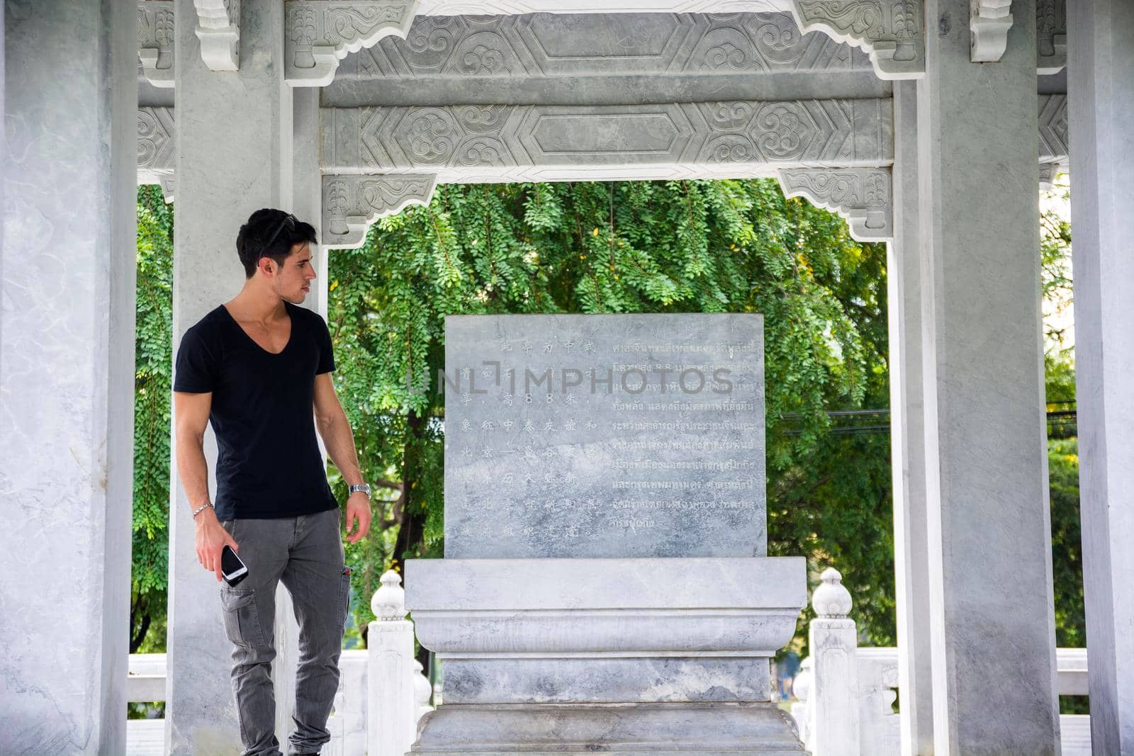 Young ethnic male tourist with dark hair in casual clothes admiring stone monument standing in Thai Chinese Friendship Pavilion located in Lumphini Park