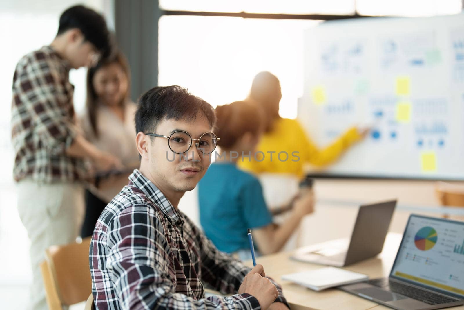 Portrait of young businessman smart casual wear looking at camera and smiling, arms crossed in modern office workplace. Young Asia guy standing in contemporary meeting room.