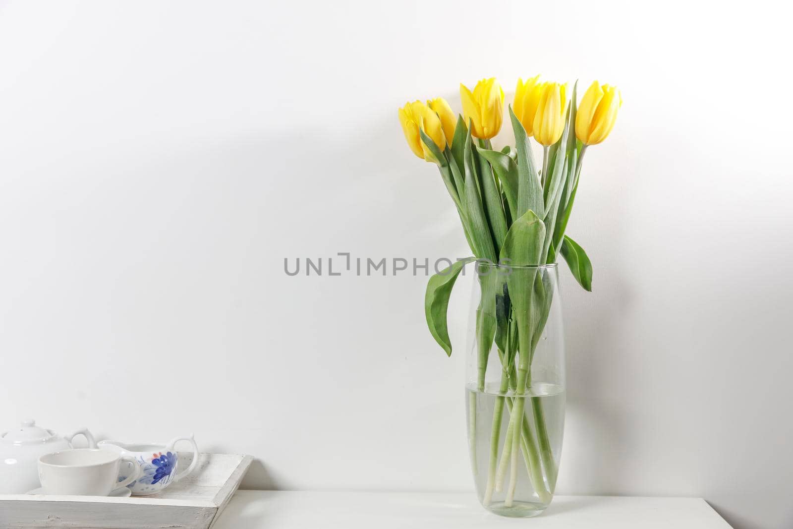 Bouquet of yellow tulip in the glass vase on white table by elenarostunova