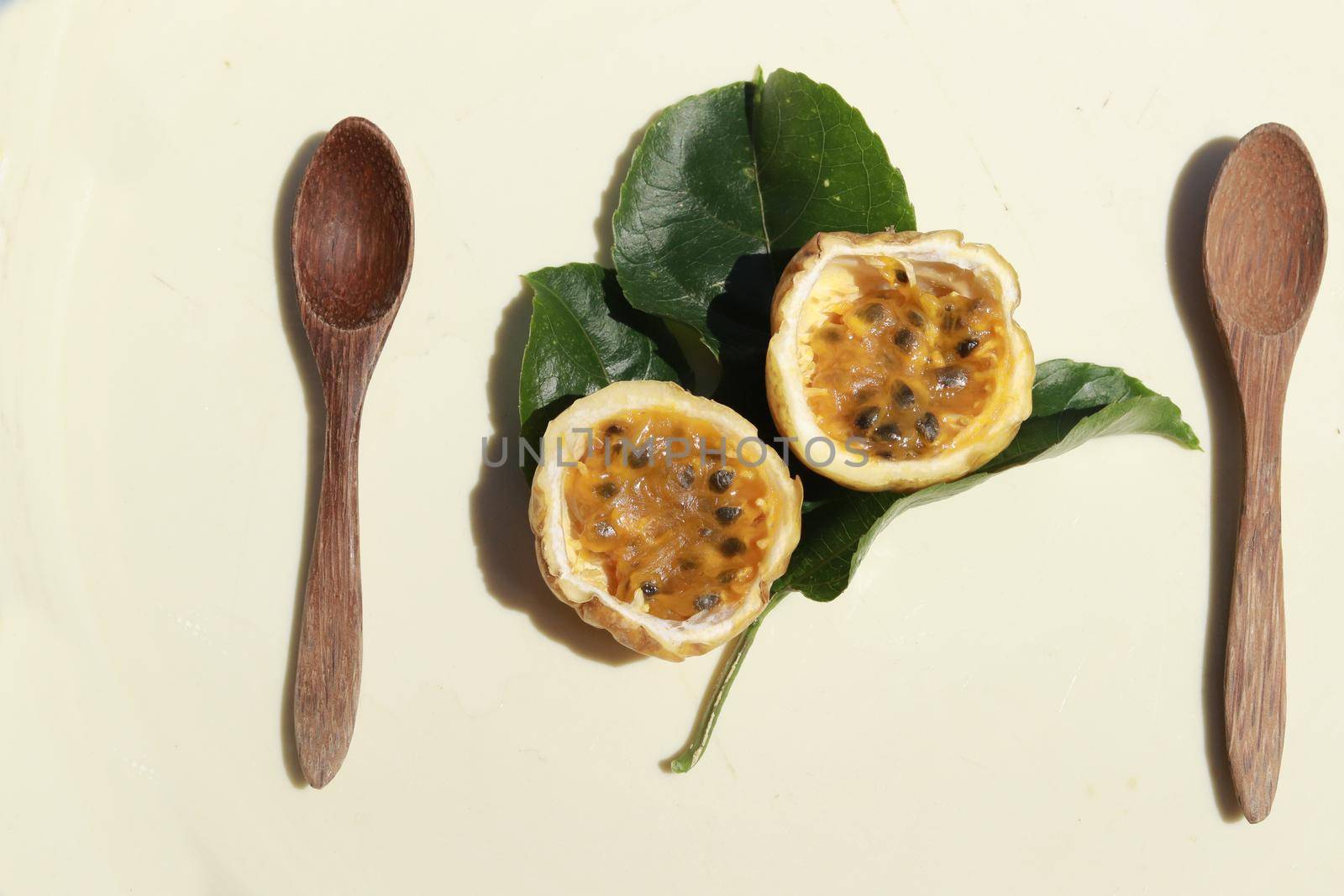 Top view of wooden spoon and yellow passion fruit sliced in half