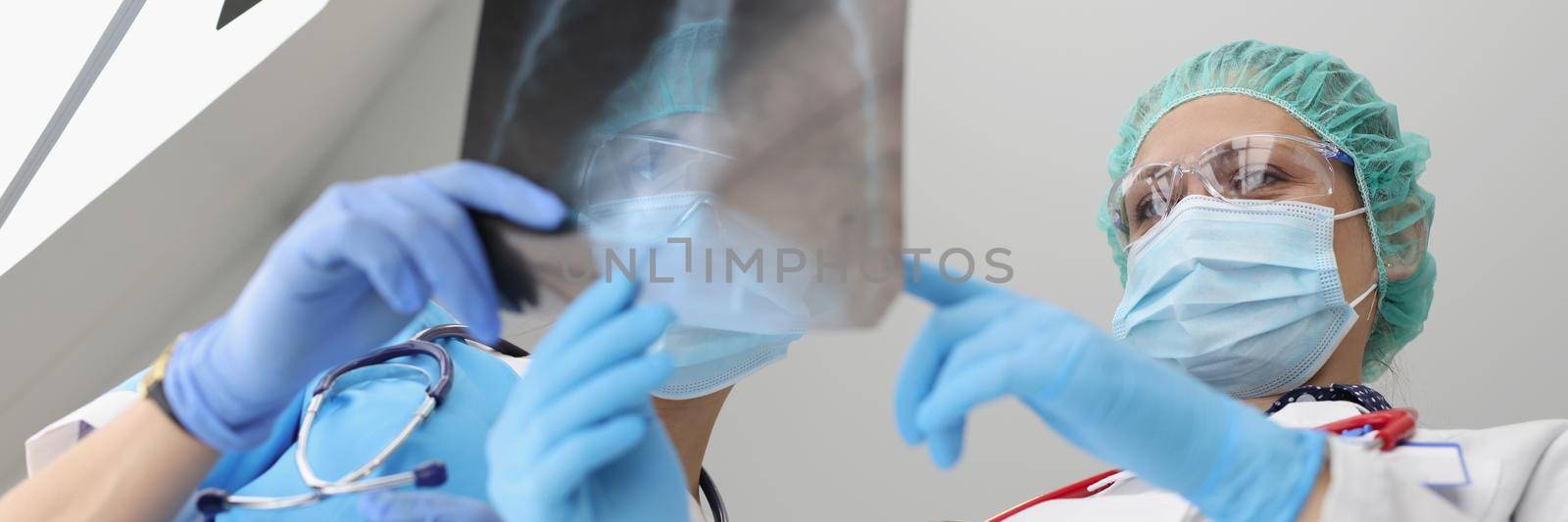 Low angle of medical workers examine x ray of patient, colleagues discuss results. Doctor holding lungs scan in clinic. Checkup, coronavirus, virus, hospital, medicine concept