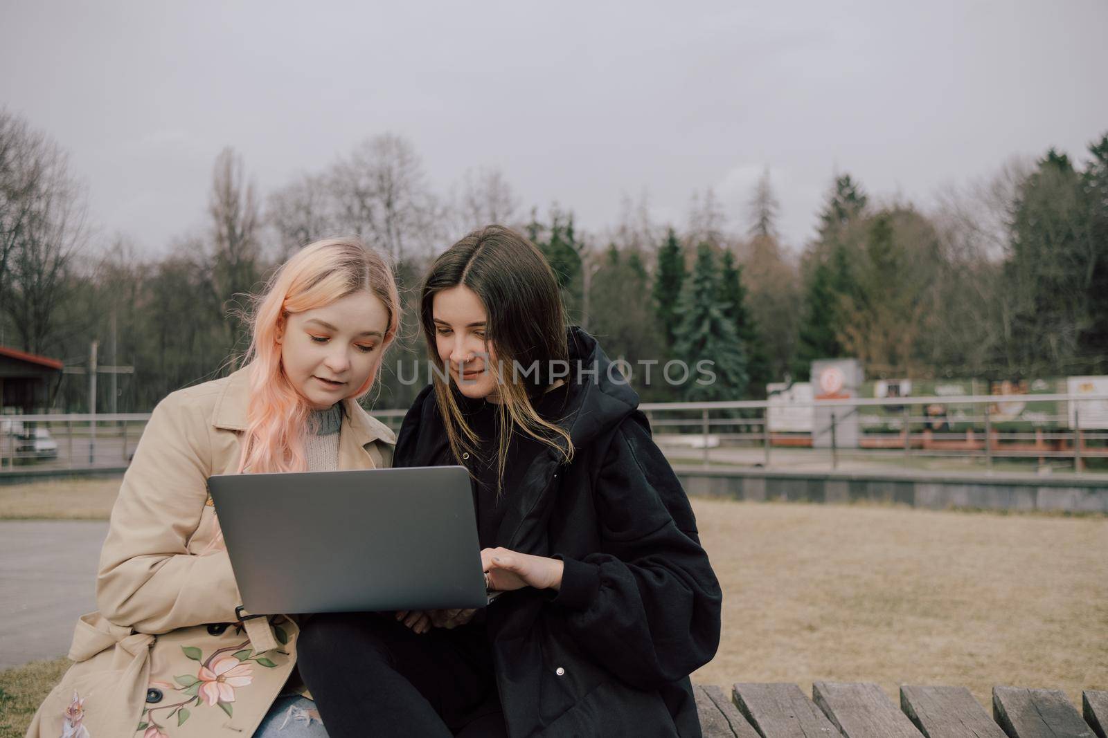 Two woman seat in the park with laptop and watch. by Symonenko