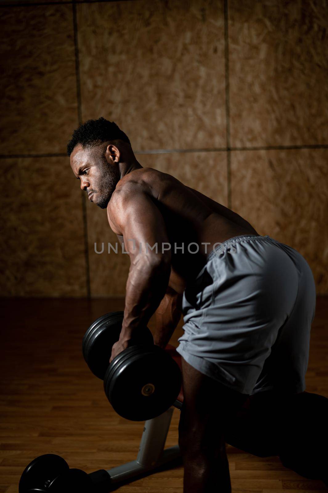African american man with naked torso doing triceps row with dumbbell on bench