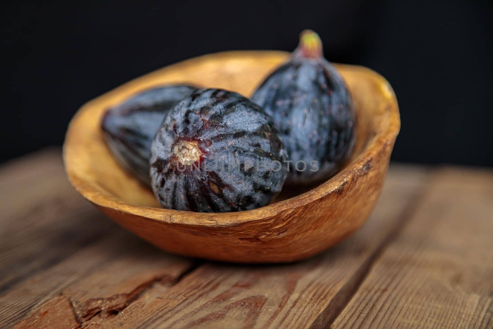Fresh purple figs in a bowl on a wooden background from old boards. Raw exotic figs. Low key