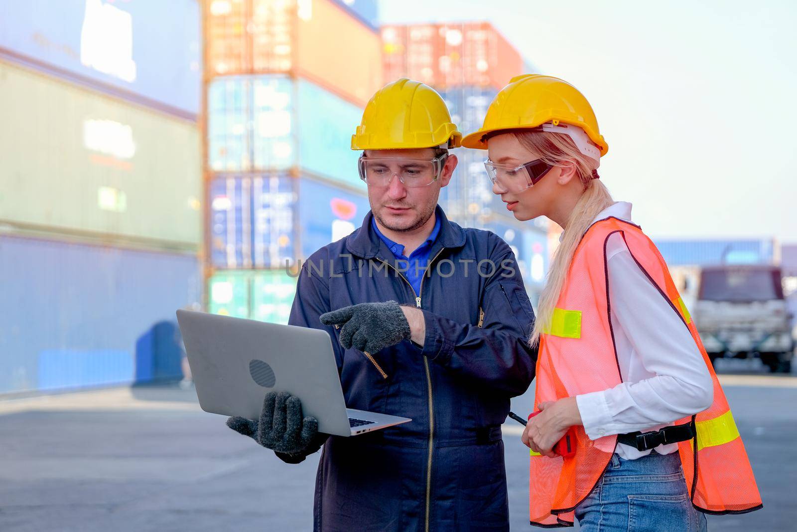 Technician worker man point to laptop and discuss with his worker woman in cargo container shipping area.