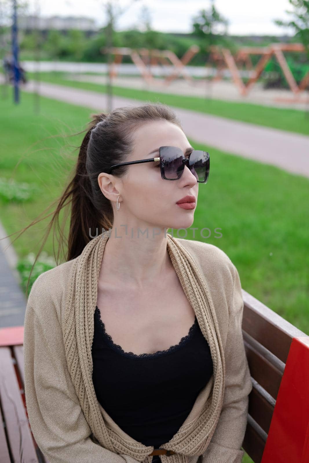 attractive brunette woman sitting on a bench in park. fashion clothes, stylish look by oliavesna