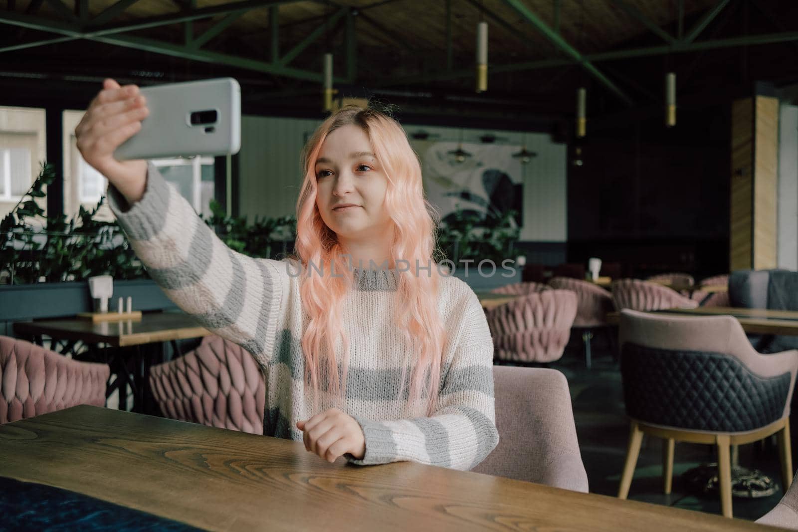 Young woman sitting in a cozy coffehouse drinking coffee and using her smartphone.