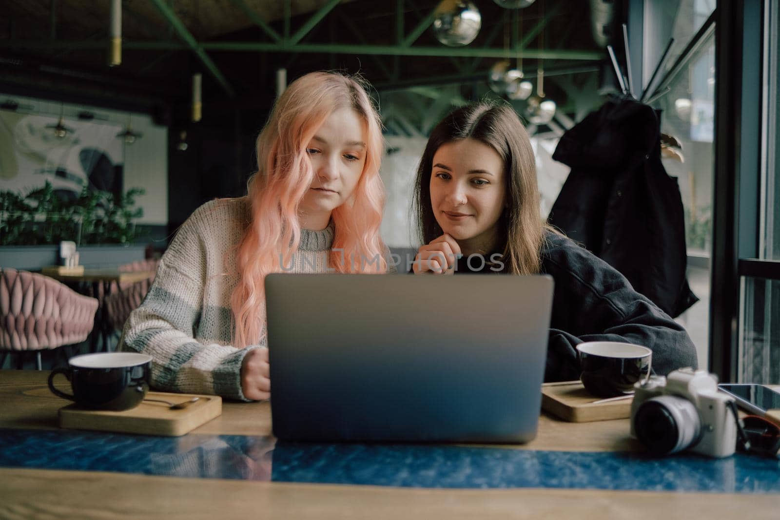 two happy young women sitting in coffee shop looking at laptop computer together.