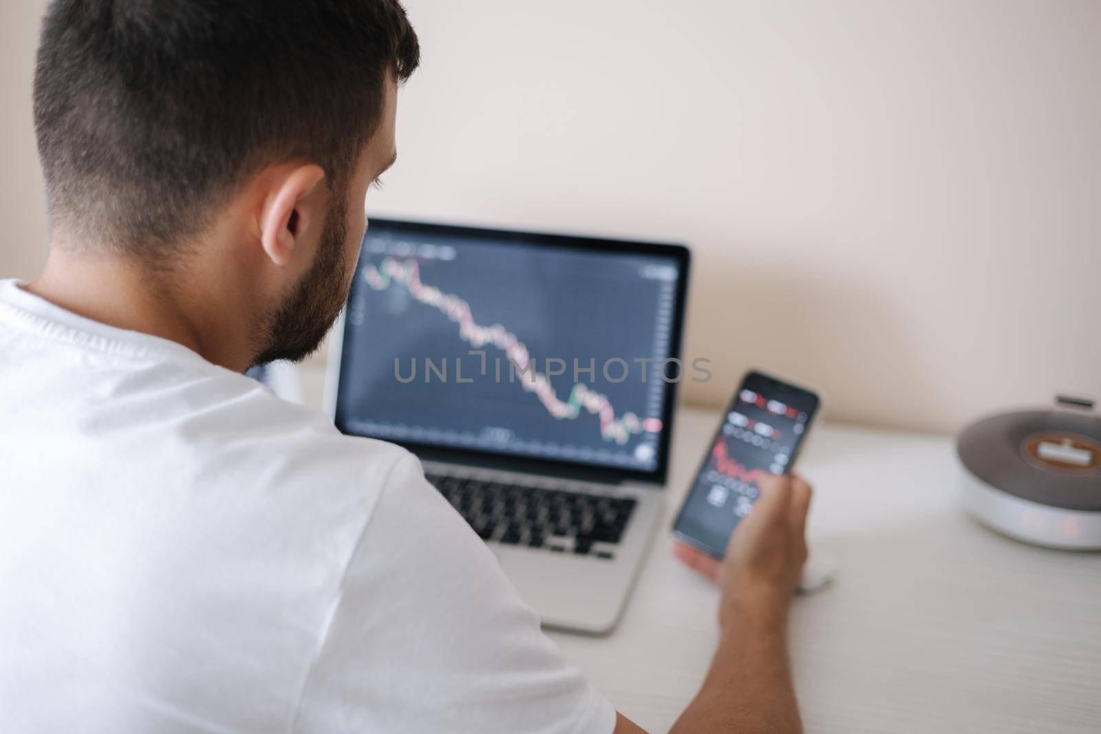 Young adult man trading on line with tablet pc connected to stock market. People, finance, investments. Over the shoulders.