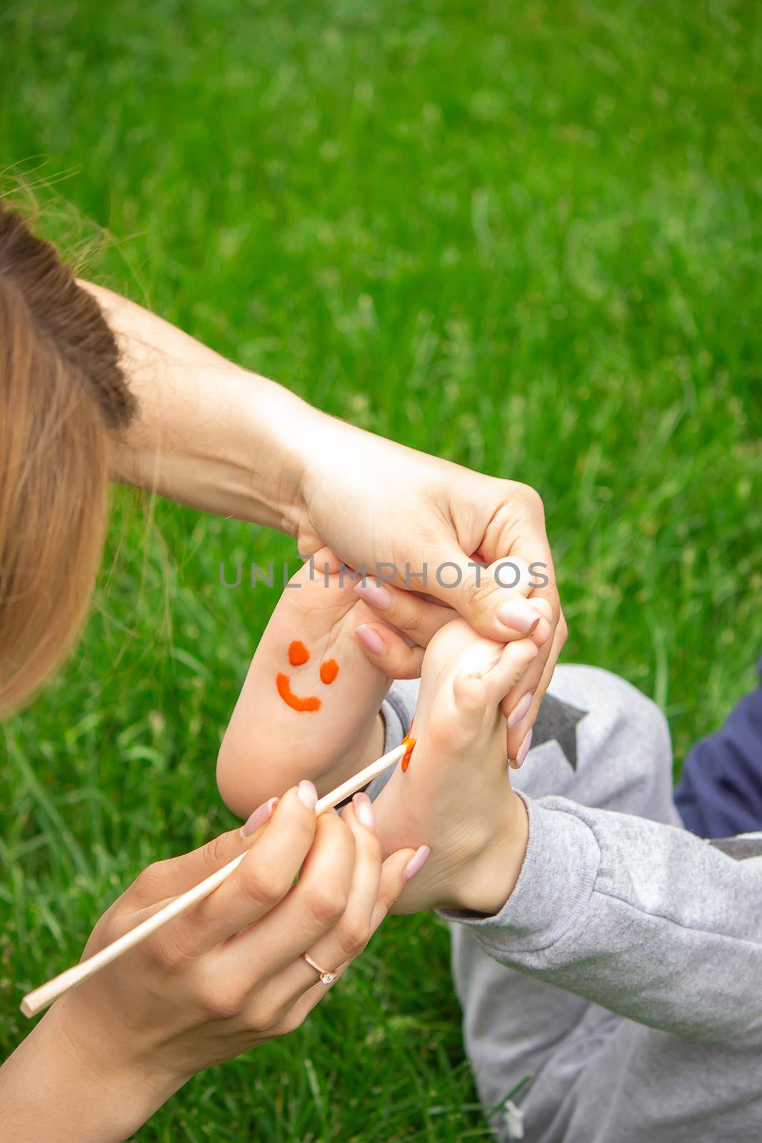 child sitting on the grass, smiling on the child's leg with paints