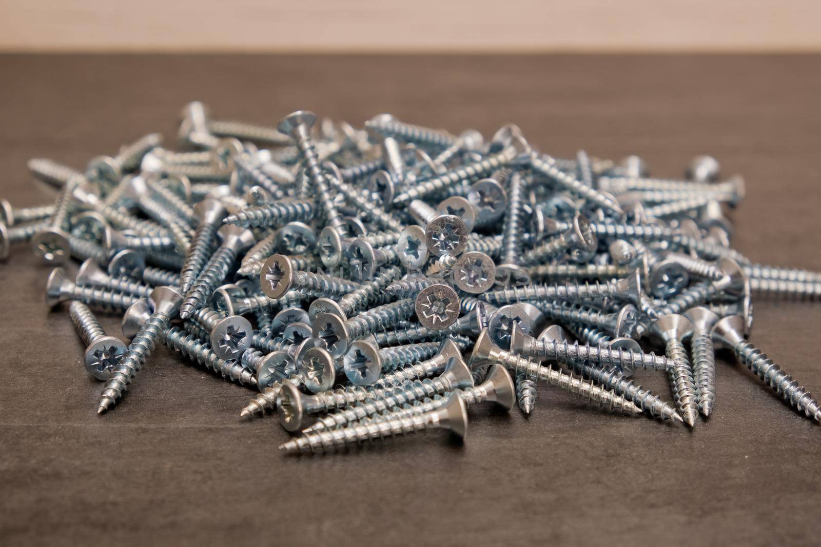 A lot of silver metal screws on the table close-up, background. Selective focus.