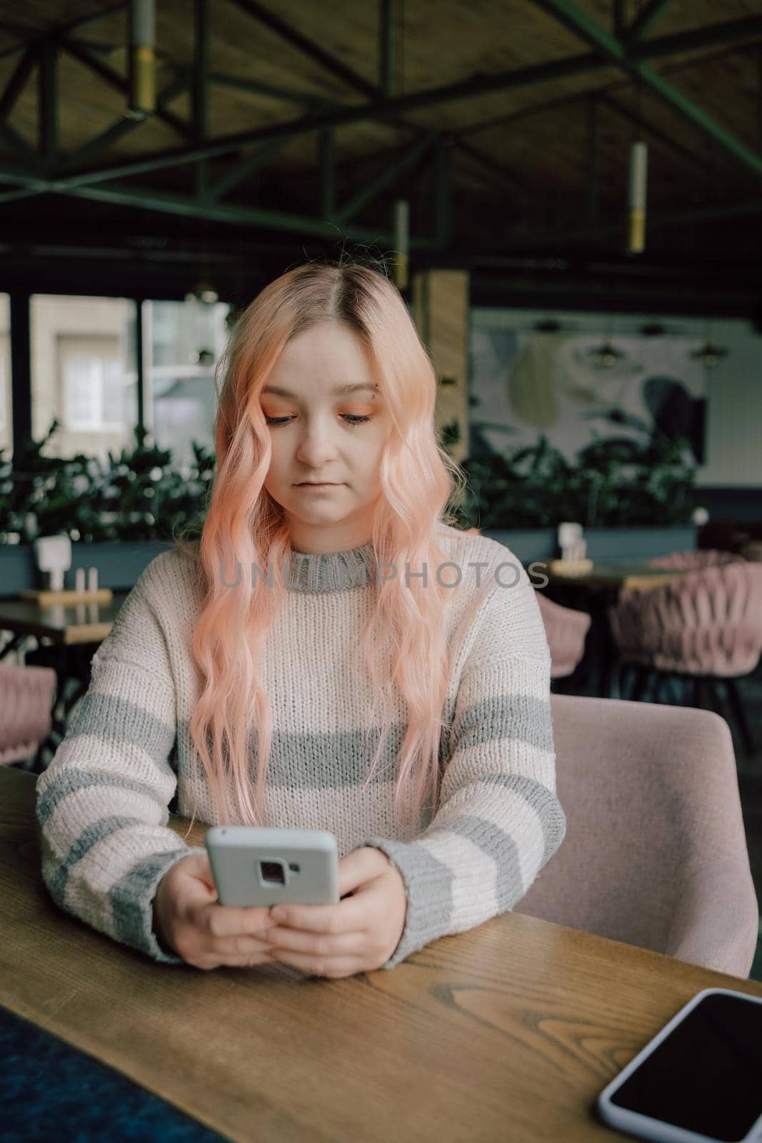 Young curious woman with pink hair likes millennial beautiful girl looking with interest watching smiling lady sitting nearby in cafe using smartphone, flirt in public place, dating and love at first sight concept