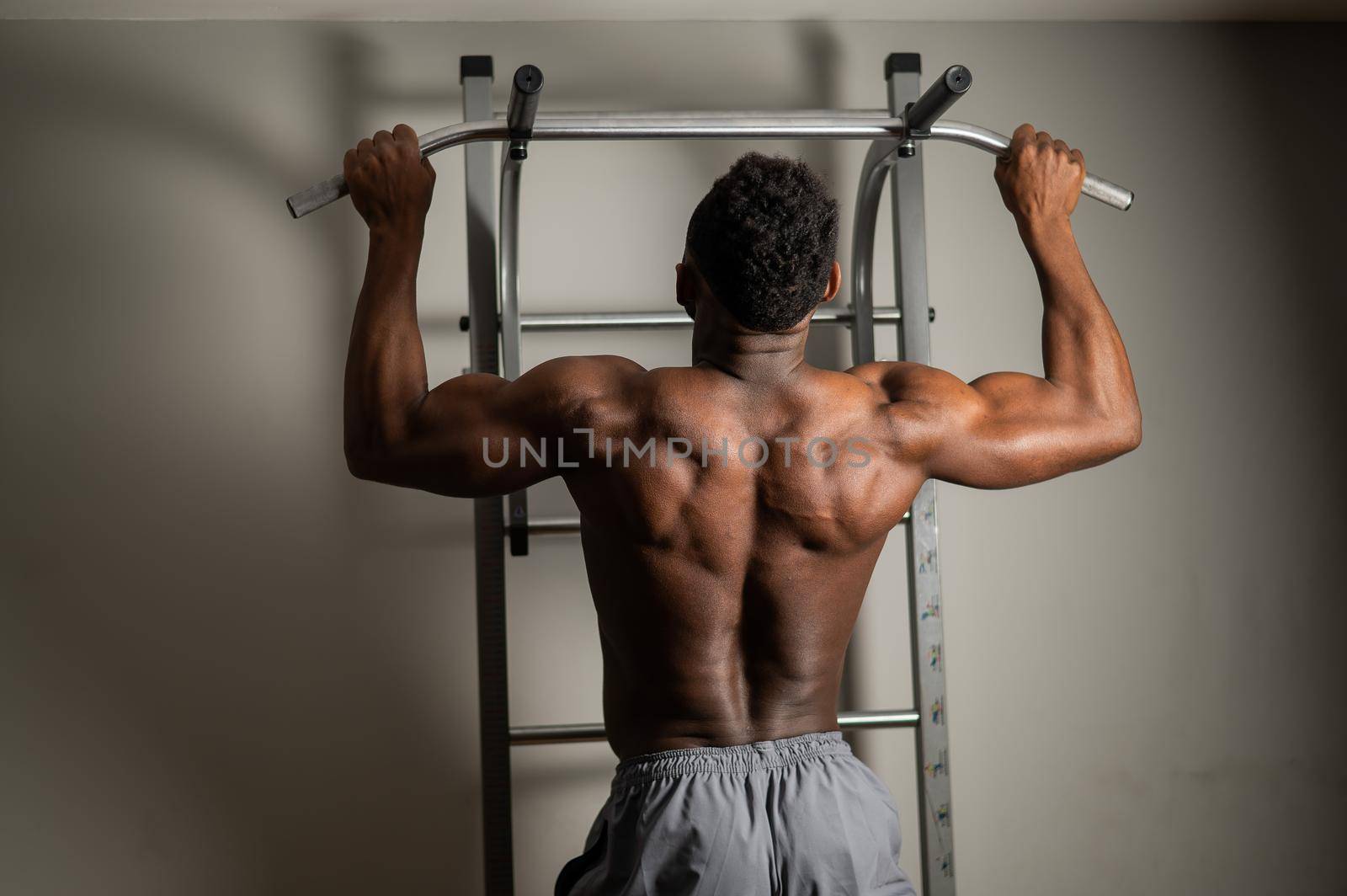 African american man with naked torso pulls up on horizontal bar in gym. by mrwed54